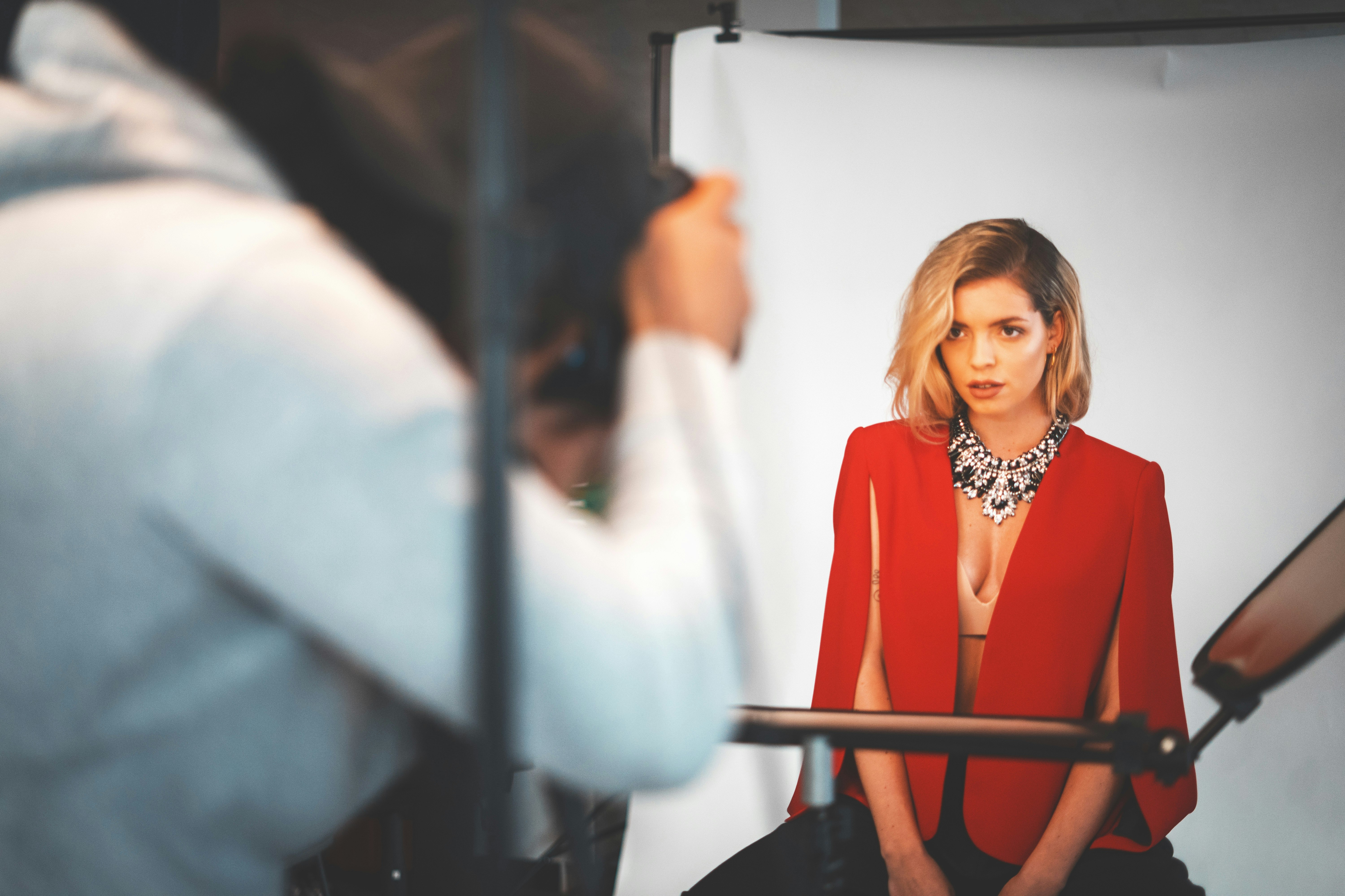 woman wearing red suit jacket sitting near white curtain